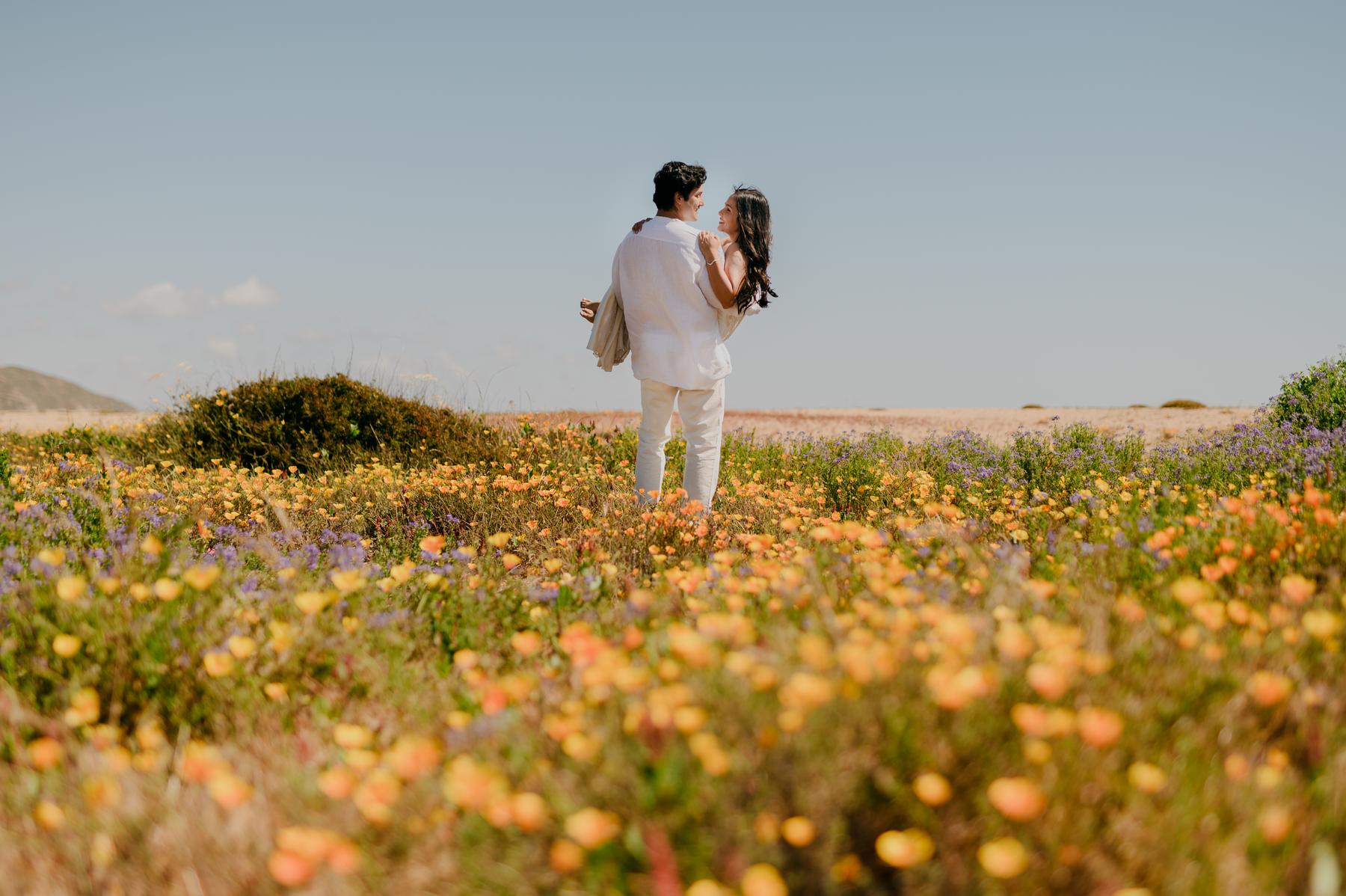 Sofía y Roberto abrazados en medio de un campo de flores, mirándose