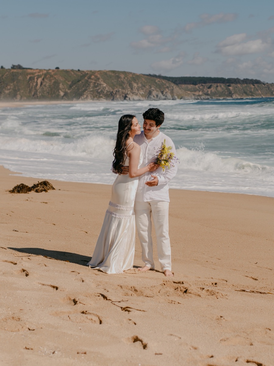 Sofía y Roberto abrazados en la orilla de la playa, ella con el ramo en la mano
