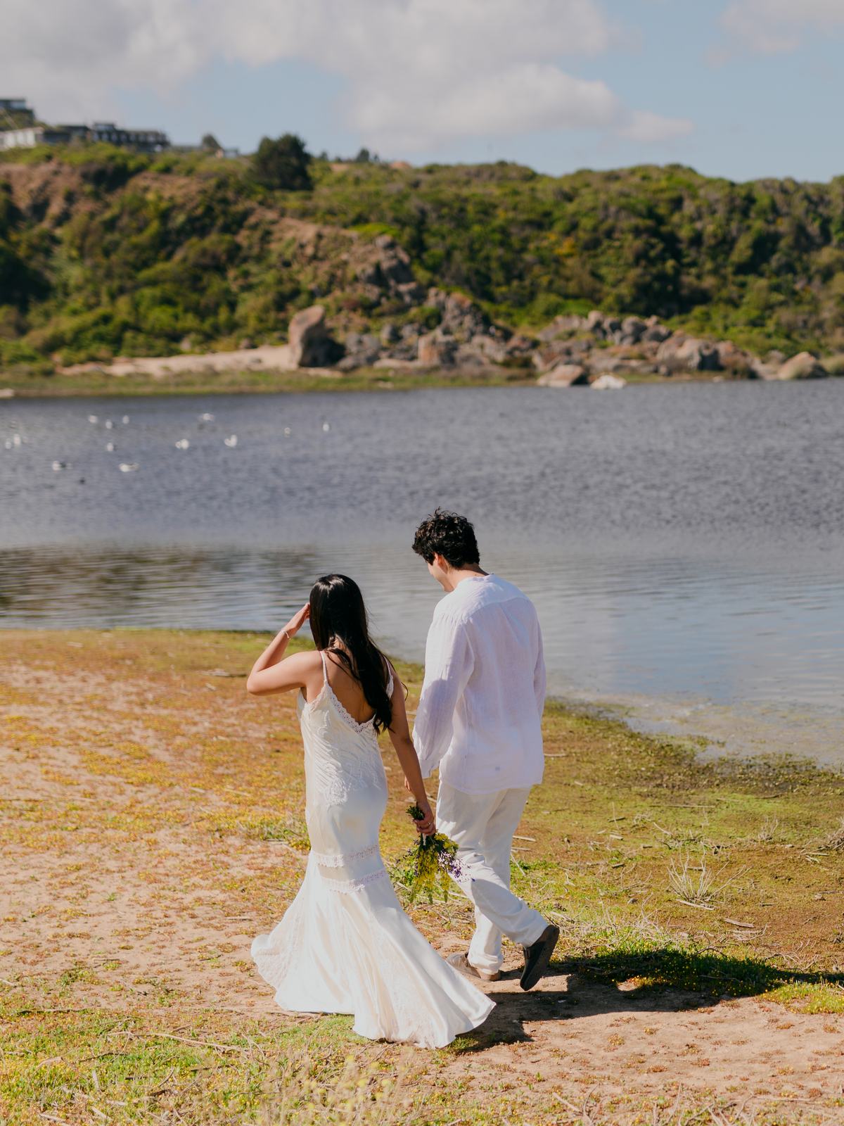 Sofía y Roberto caminando de la mano junto a una laguna, ella con el ramo en la mano